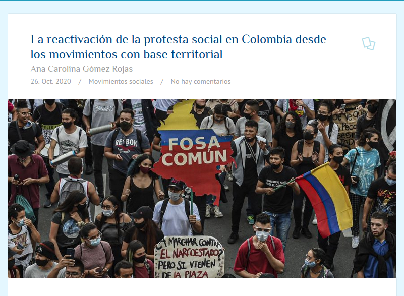 Manifestación en Colombia con participantes usando mascarillas. Se sostiene un cartel que dice 'FOSA COMÚN' y hay una bandera de Colombia.